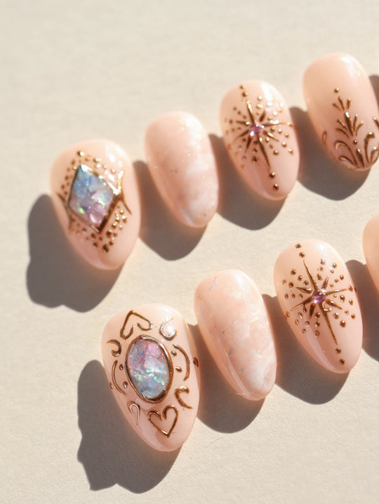 Blush Crown celestial press-on nails laid out with blush nude marbling, gold line art, and iridescent crystal accents