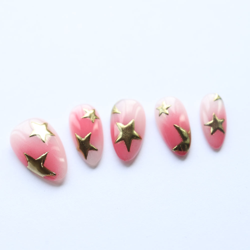 Blush Star press-on nails laid out with pink gradient and metallic gold star accents