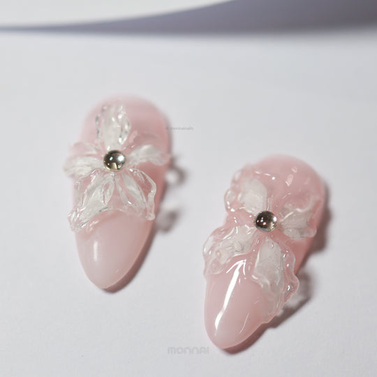 Blushing Petals press-on nails laid out, sheer blush pink with 3D white flowers and pearl accents