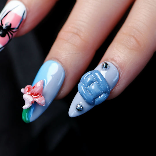 Bold Fantasy press-on nails on hand with blue 3D block, pink flower, silver studs, and spider art in indie maximalist style
