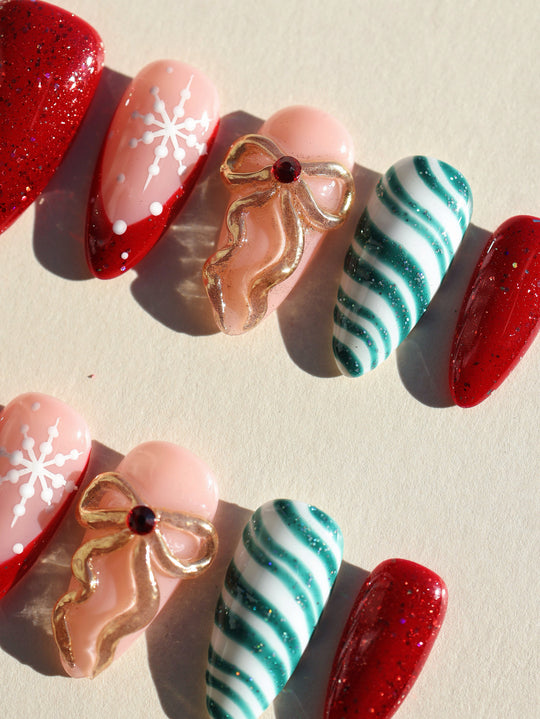 Candy Ribbon press-on nails laid out with red glitter, snowflakes, gold bows, and teal striped tips