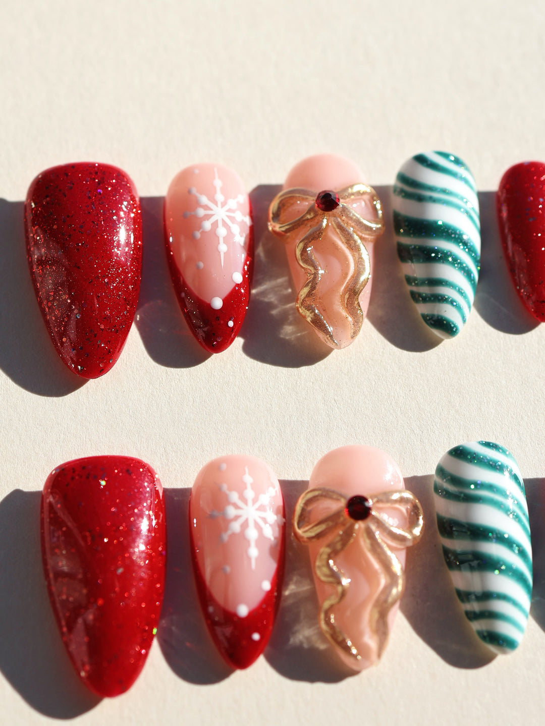 Candy Ribbon press-on nails set with red glitter, white snowflakes, gold bow and green striped tips