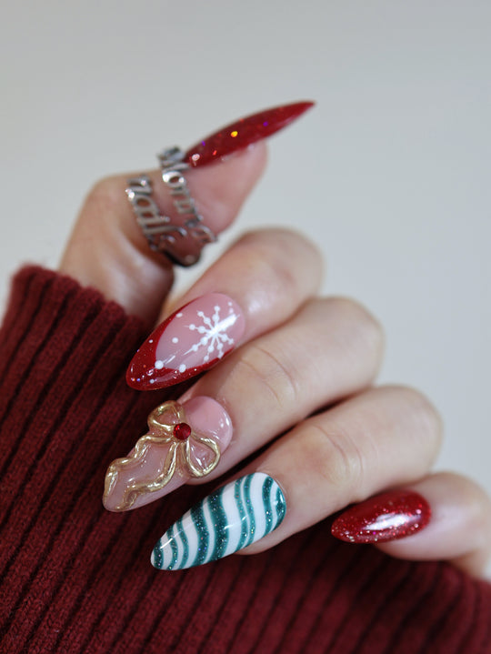 Candy Ribbon press-on nails on hand with red glitter tips, snowflake art, gold bow, and teal candy-cane stripes