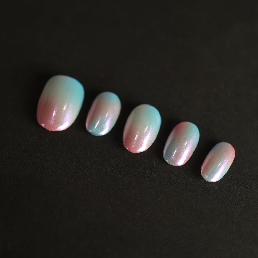 Candy Sky press-on nails laid out with pastel blue-to-peach ombre and iridescent pearl shine