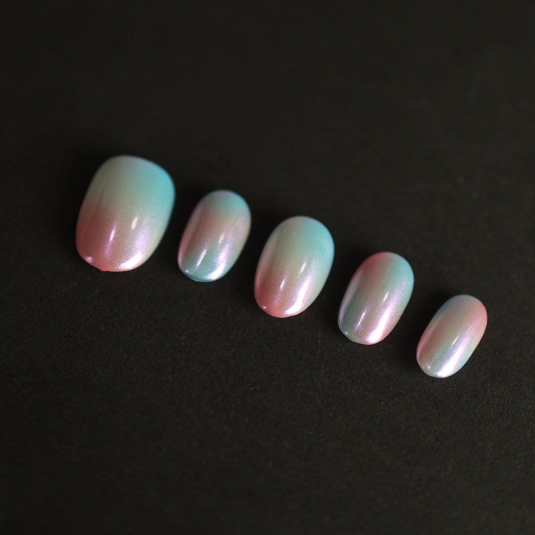 Candy Sky press-on nails laid out with pastel blue-to-peach ombre and iridescent pearl shine