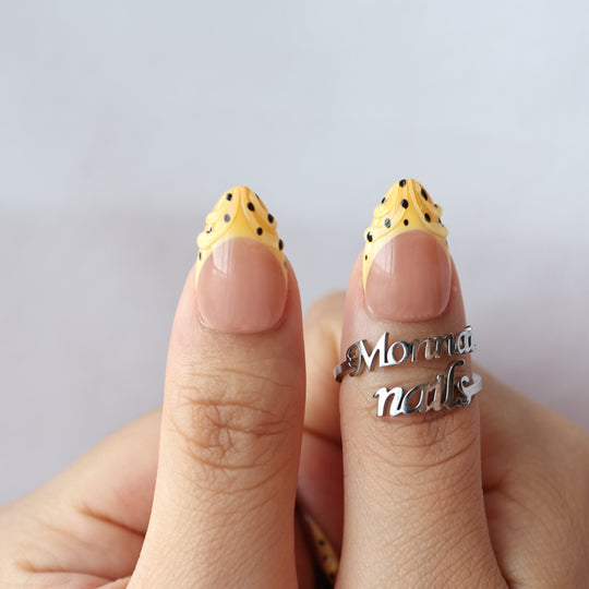 Caramel Dots press-on nails worn on hands, with butter yellow wavy French tips and black polka dots.