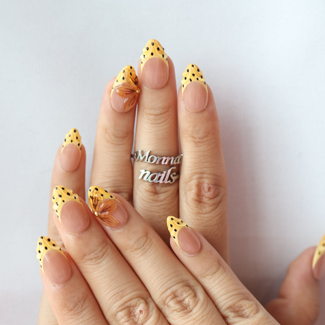 Caramel Dots press-on nails worn on hands, with butter yellow polka dot French tips and amber flower accents.