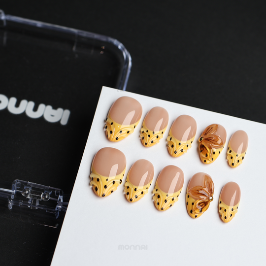 Caramel Dots press-on nails laid out with butter yellow wavy French tips, black polka dots, and amber flower accents