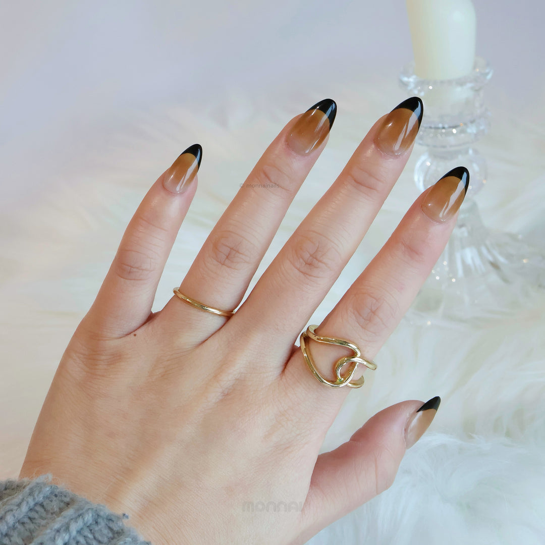Caramel Edge press-on nails on hand, warm nude base with crisp black French tips and glossy shine
