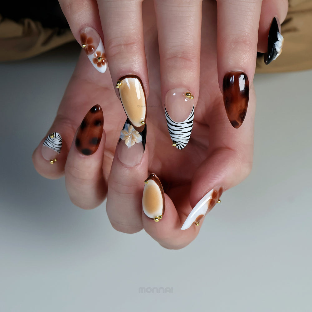 Caramel Flora press-on nails worn on hand, with tortoiseshell brown, zebra tips, hand-painted florals and gold beads.