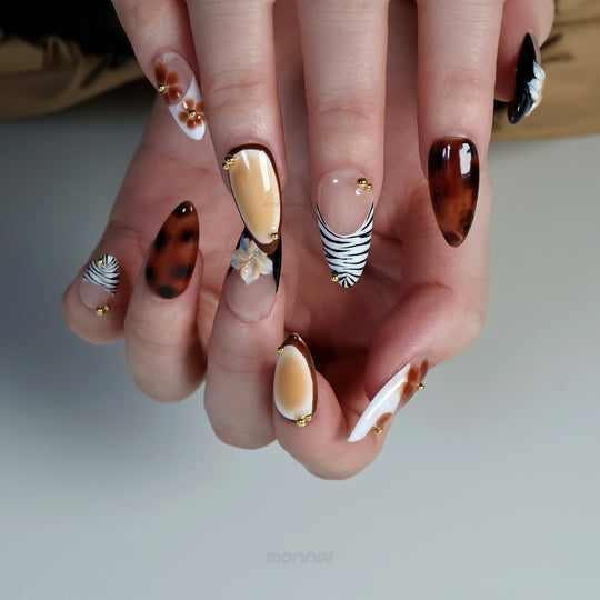 Caramel Flora press-on nails worn on hand, with tortoiseshell brown, zebra tips, hand-painted florals and gold beads.