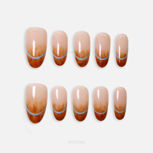 Caramel Mist press-on nails in a modern tortoiseshell theme, shown laid out with nude bases, amber marble tips, and light blue arches.