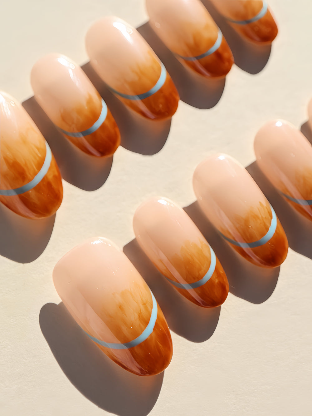 Caramel Mist press-on nails laid out in a close-up, showing nude bases with amber marble tips and light blue arches.