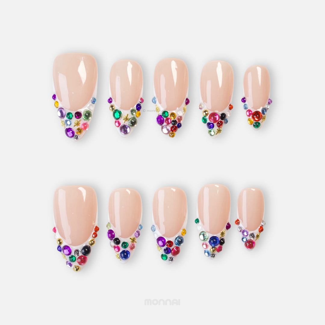 Carnival Lights press-on nails with rainbow crystals, gold star accents, and a glossy nude base shown in a flat lay