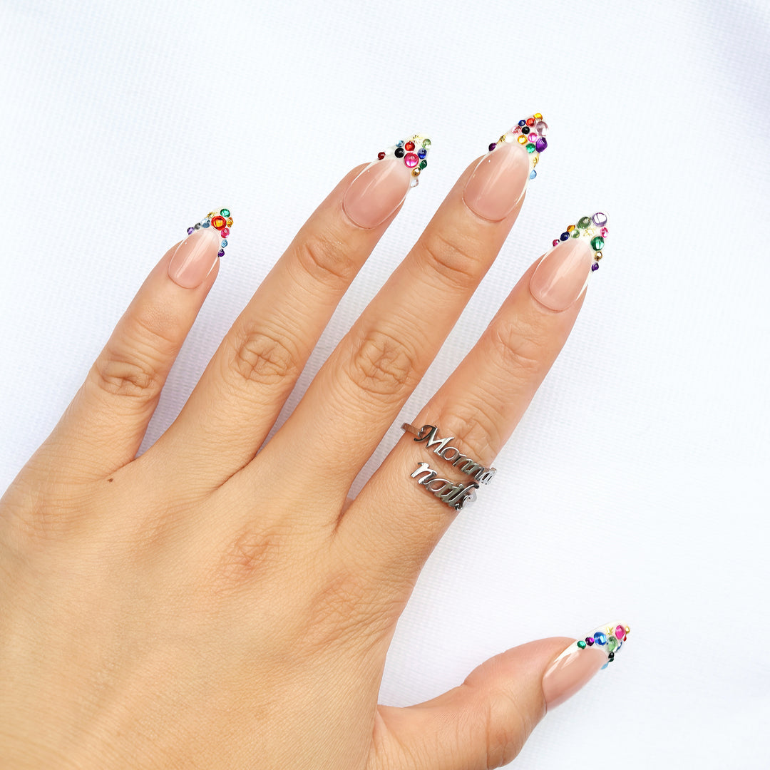 Carnival Lights press-on nails on hand, nude jelly French tips with rainbow crystals and gold star accents.