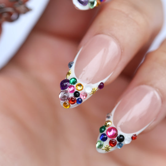 Carnival Lights press-on nails in close-up, white French tips with rainbow crystals and gold star accents