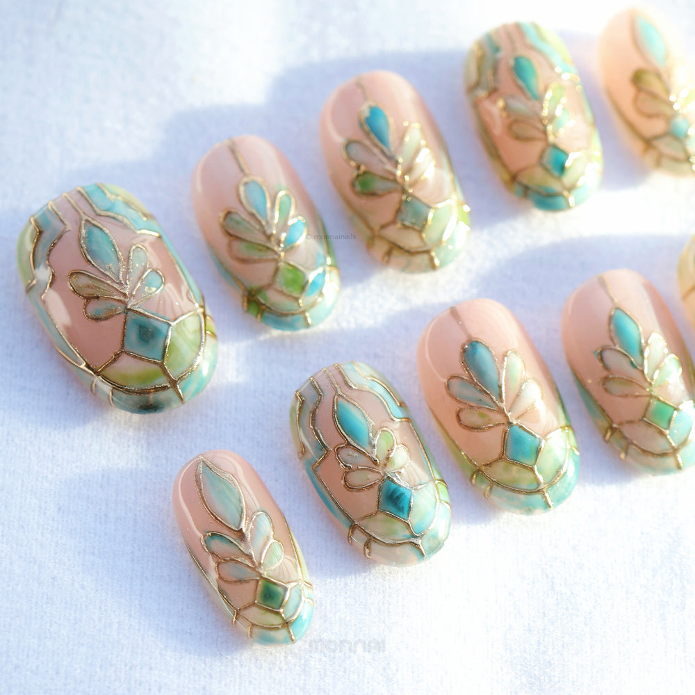 Cathedral Bloom press-on nails laid out in a stained-glass pattern with soft nude, pale blue, sage, and gold lines