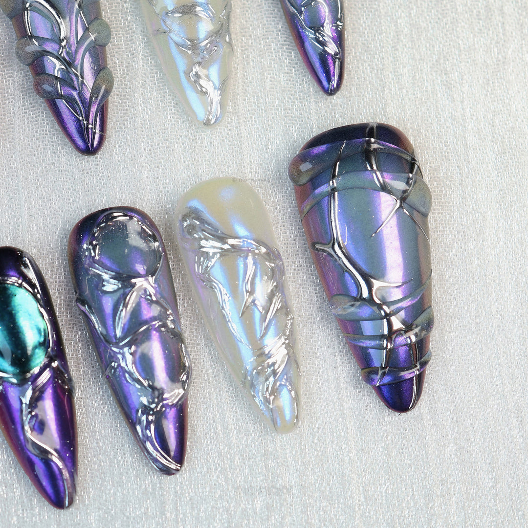 Celestial Aurora press-on nails laid out in close-up, iridescent purple, blue and white with silver chrome detailing.