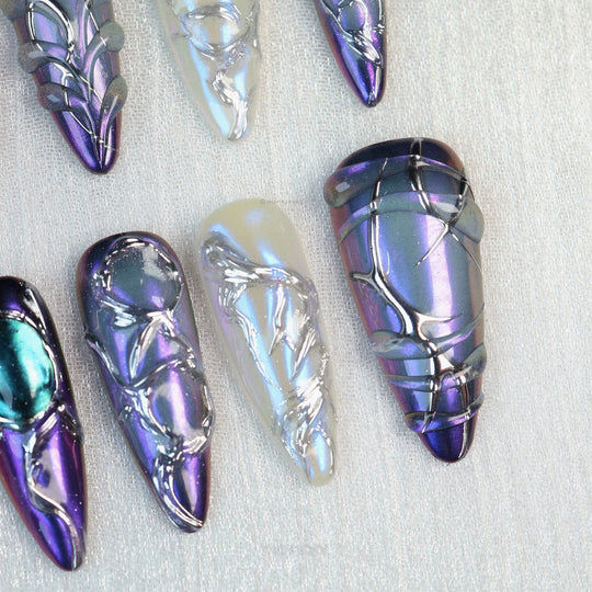 Celestial Aurora press-on nails laid out in close-up, iridescent purple, blue and white with silver chrome detailing.