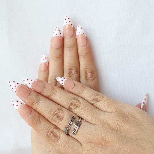 Cherry Pop press-on nails worn on hands, nude pink French tips with white, red polka dots and a glossy finish.