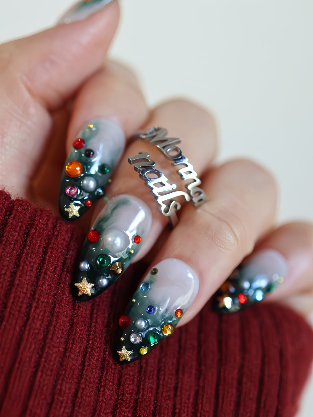 Christmas Tree press-on nails worn on hand with emerald gradient, colorful gems, pearls, and gold star charms