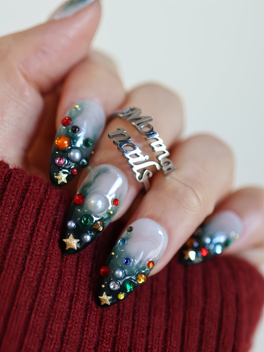Christmas Tree press-on nails worn on hand with emerald gradient, colorful gems, pearls, and gold star charms