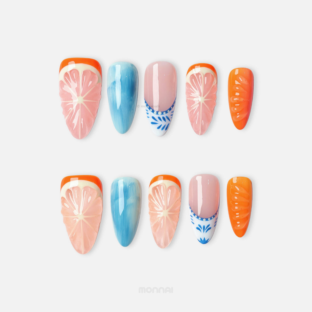 Citrus Porcelain press-on nails laid out with grapefruit slices, ocean blue fades, and bright orange accents on nude.