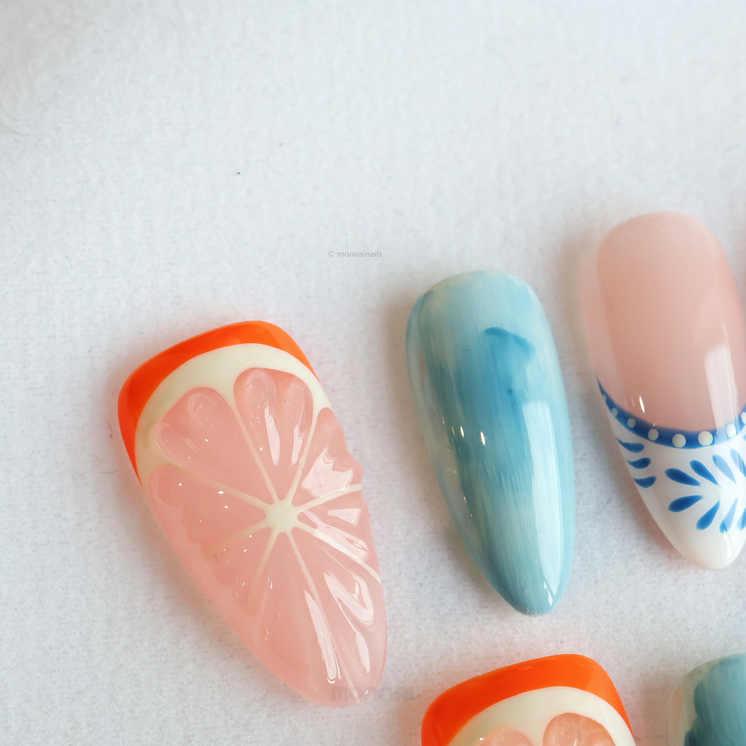 Citrus Porcelain press-on nails in close-up, with grapefruit slice detail, ocean blue fade, and nude glossy finish.