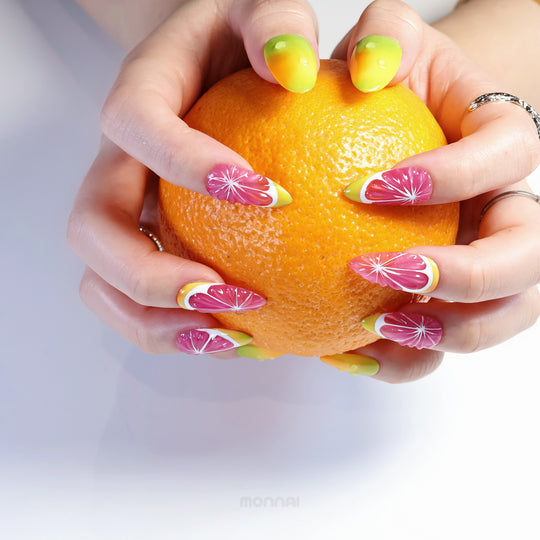 Citrus Splash press-on nails worn on hands holding an orange, with glossy pink citrus slice details and yellow-green tips