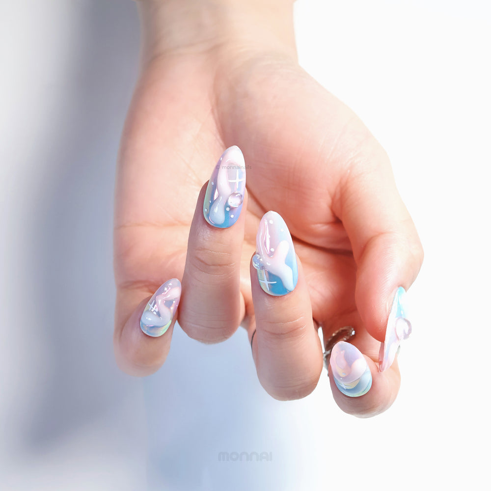Cloud Dream press-on nails worn on hand, with blue-pink aura fades, glossy chrome shine, and rounded gem accents.