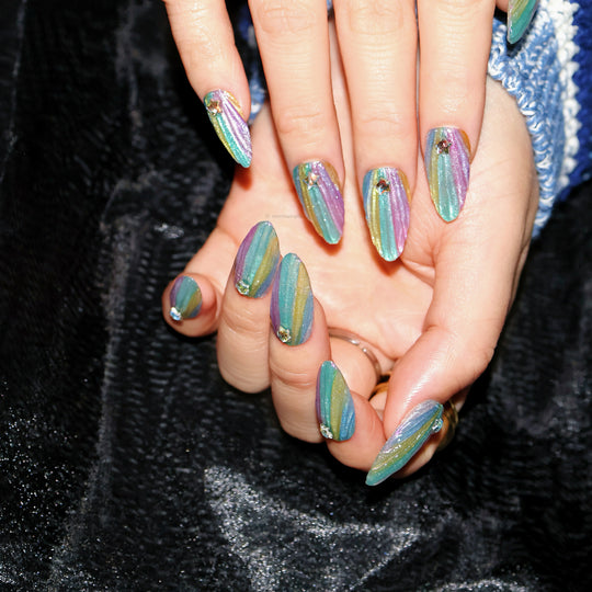 Cosmic Glow press-on nails worn on hand, with pastel iridescent stripes, star rhinestones, and a glossy finish.