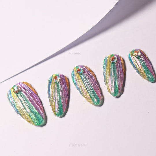 Cosmic Glow press-on nails laid out with 3D seashell texture, iridescent teal, pink and gold shimmer, each with a star rhinestone.