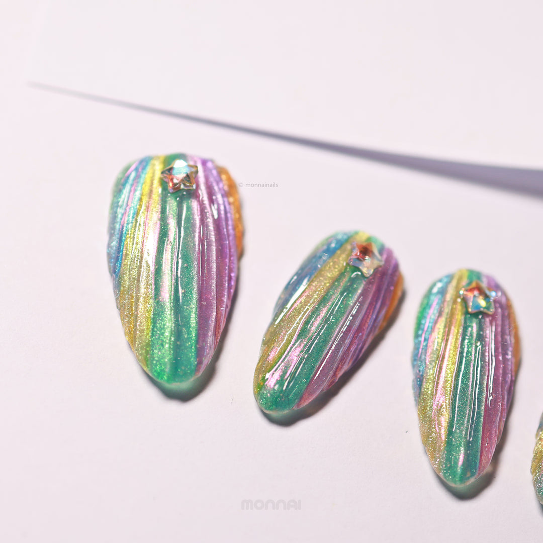 Cosmic Glow press-on nails laid out in close-up with 3D seashell texture, iridescent teal, pink and gold, star rhinestones