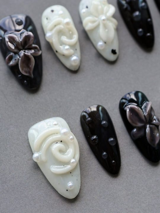 Cream Puff press-on nails laid out in glossy black and milky white, with 3D flowers, pearls, and star accents.