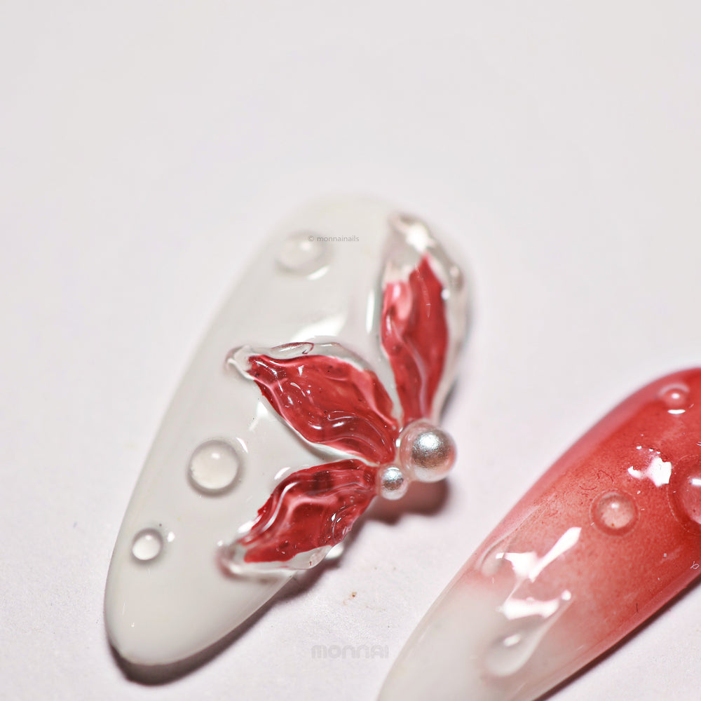 Crimson Bloom press-on nails laid out in close-up, with blood red ombre, translucent 3D flower and clear water drop details.