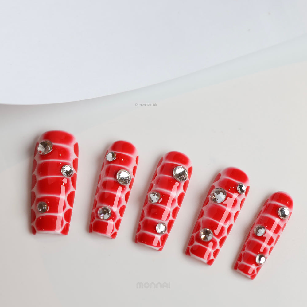 Crocodile Chic press-on nails in red crocodile texture with clear rhinestones laid out in close-up