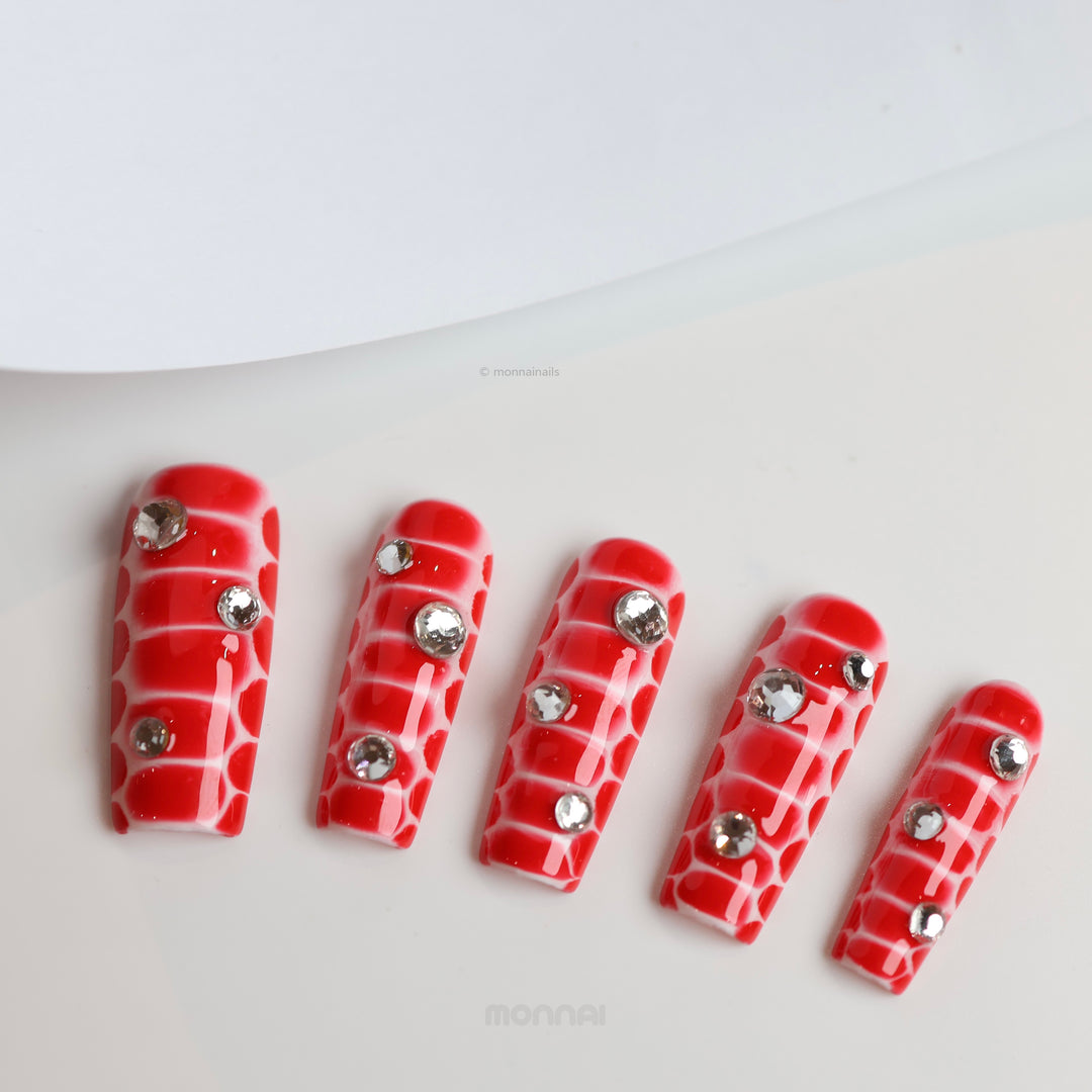 Crocodile Chic press-on nails in red crocodile texture with clear rhinestones laid out in close-up