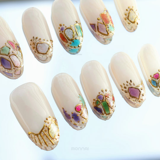 Crown Jewels press-on nails in close-up, sheer nude bases with mosaic-style accents and fine gold outlining