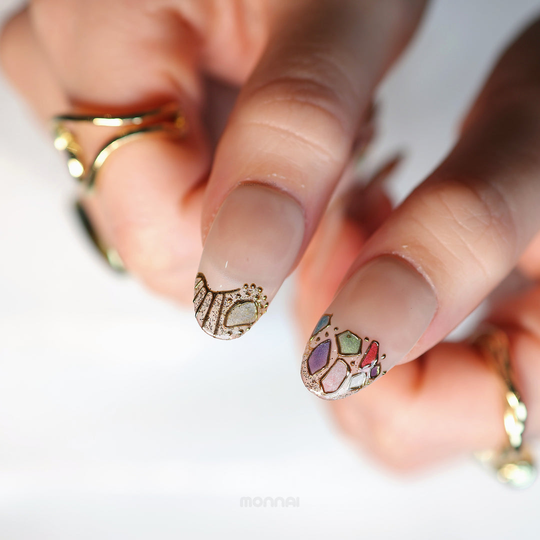 Crown Jewels press-on nails in close-up, sheer nude with mosaic-style accents and gold outlining