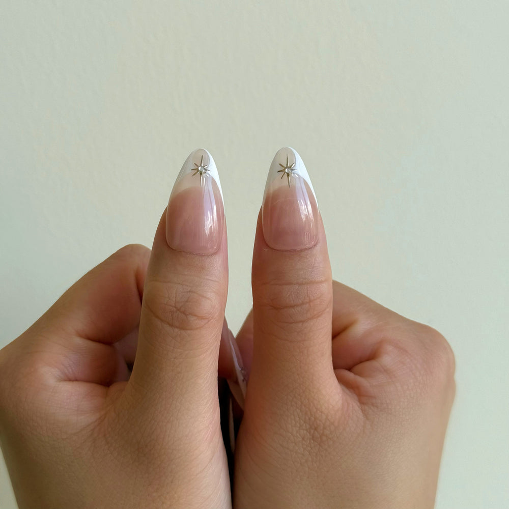 Crystal Bite press-on nails worn on hands, nude French tips with silver starburst charms