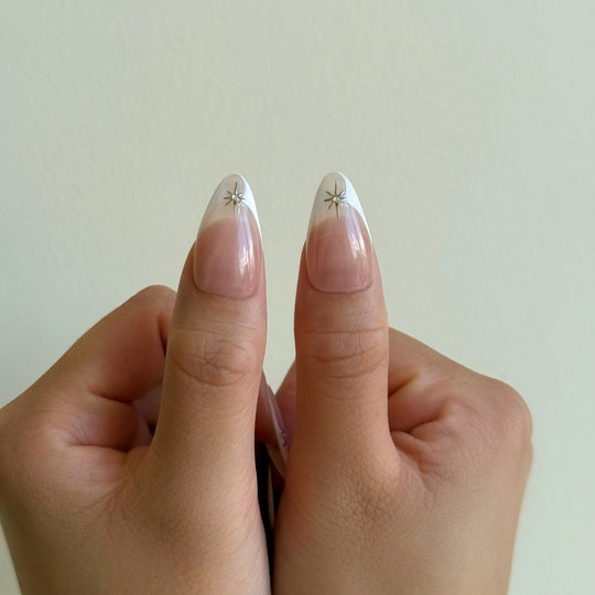 Crystal Bite press-on nails worn on hands, nude French tips with silver starburst charms
