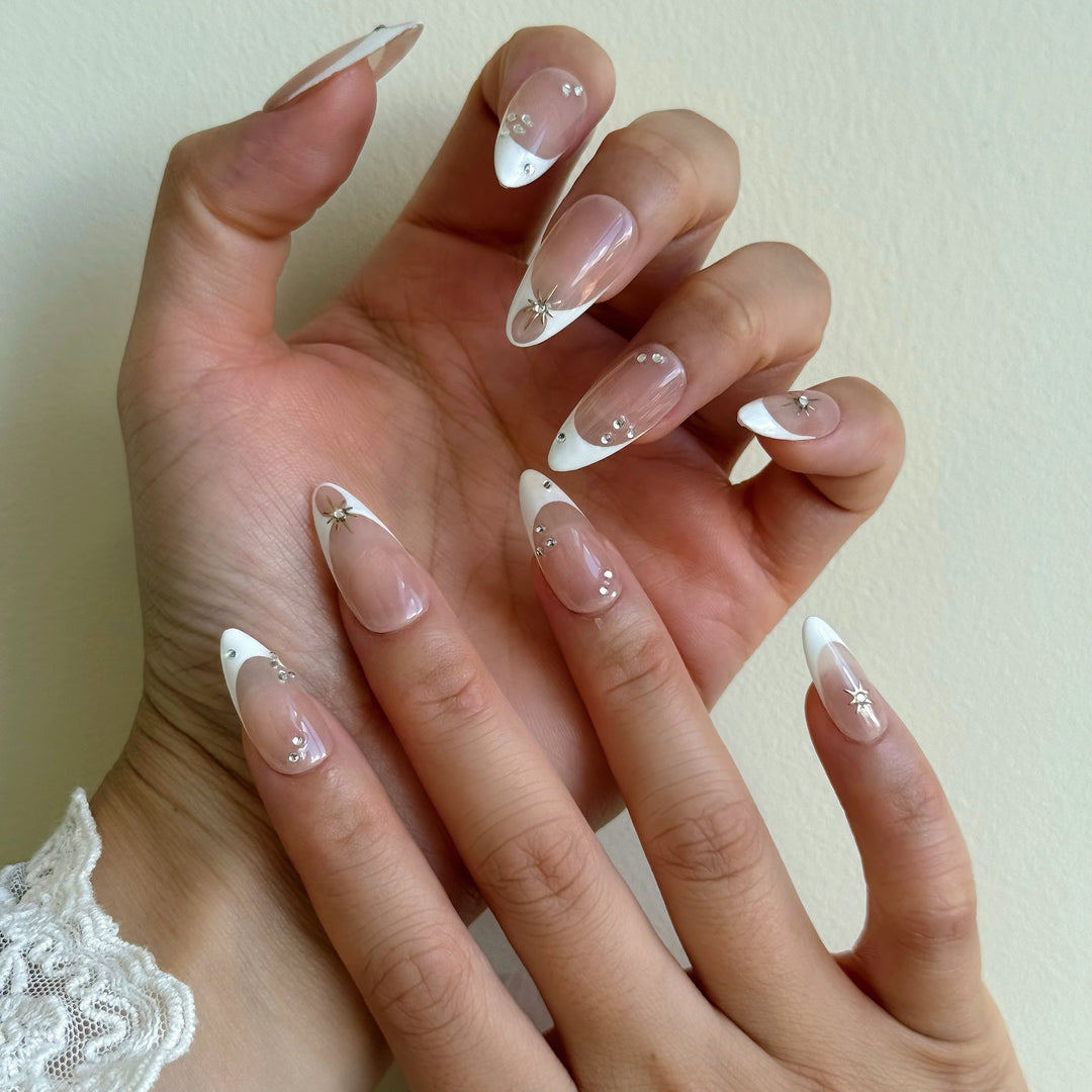 Crystal Bite press-on nails on hand, nude French tips with silver starburst charms and crystal accents