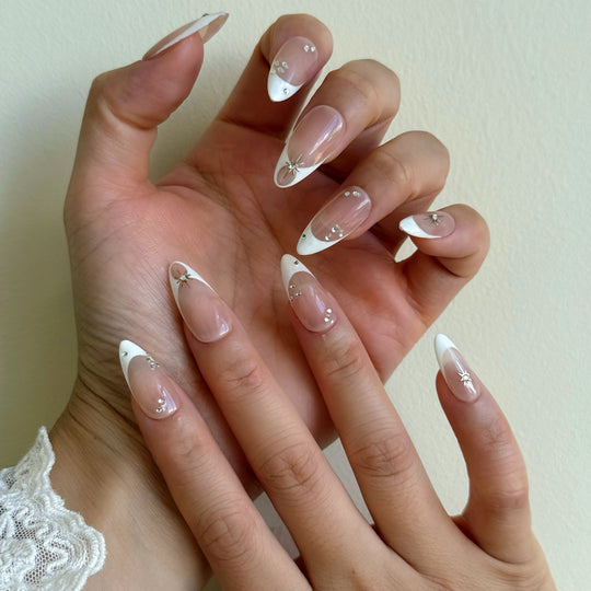 Crystal Bite press-on nails on hand, nude French tips with silver starburst charms and crystal accents