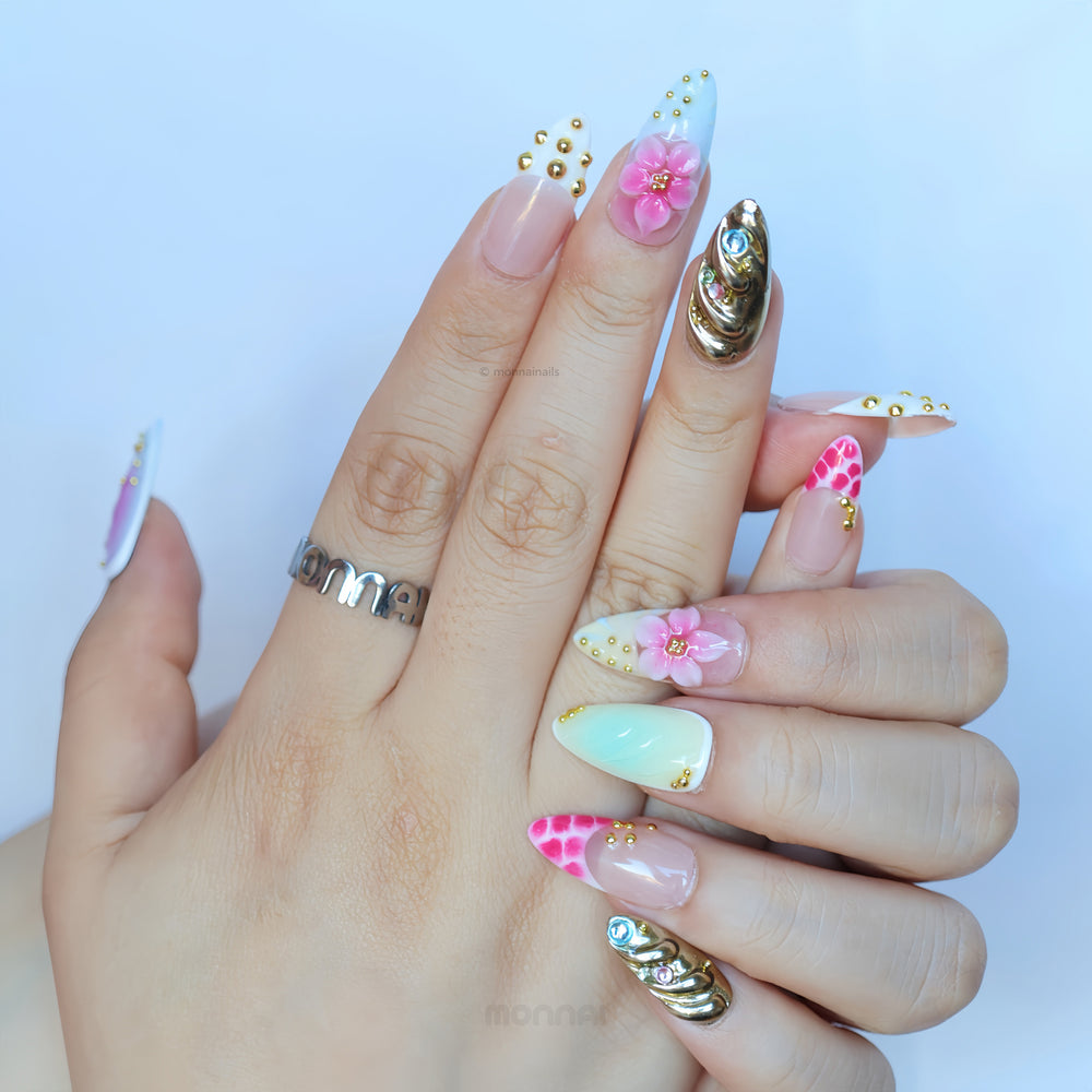 Cyber Sakura press-on nails worn on hands, with pastel ombré, pink 3D floral details, gold studs, and silver chrome accents.