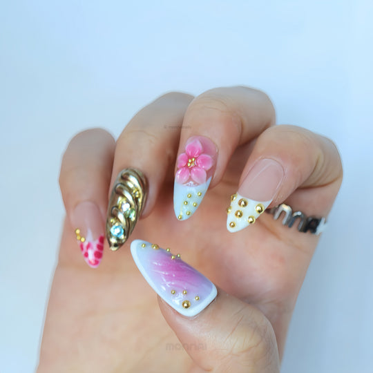 Cyber Sakura press-on nails worn on hand, pastel ombré with pink 3D floral detail, gold studs, and a silver chrome accent