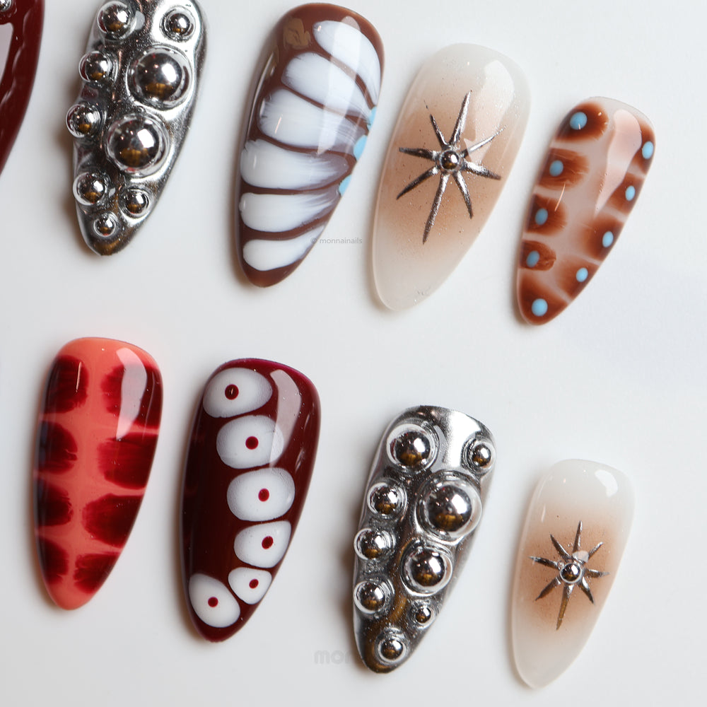 Dark Elegance press-on nails laid out with chrome spheres, crocodile-print, starburst and red-brown graphic accents