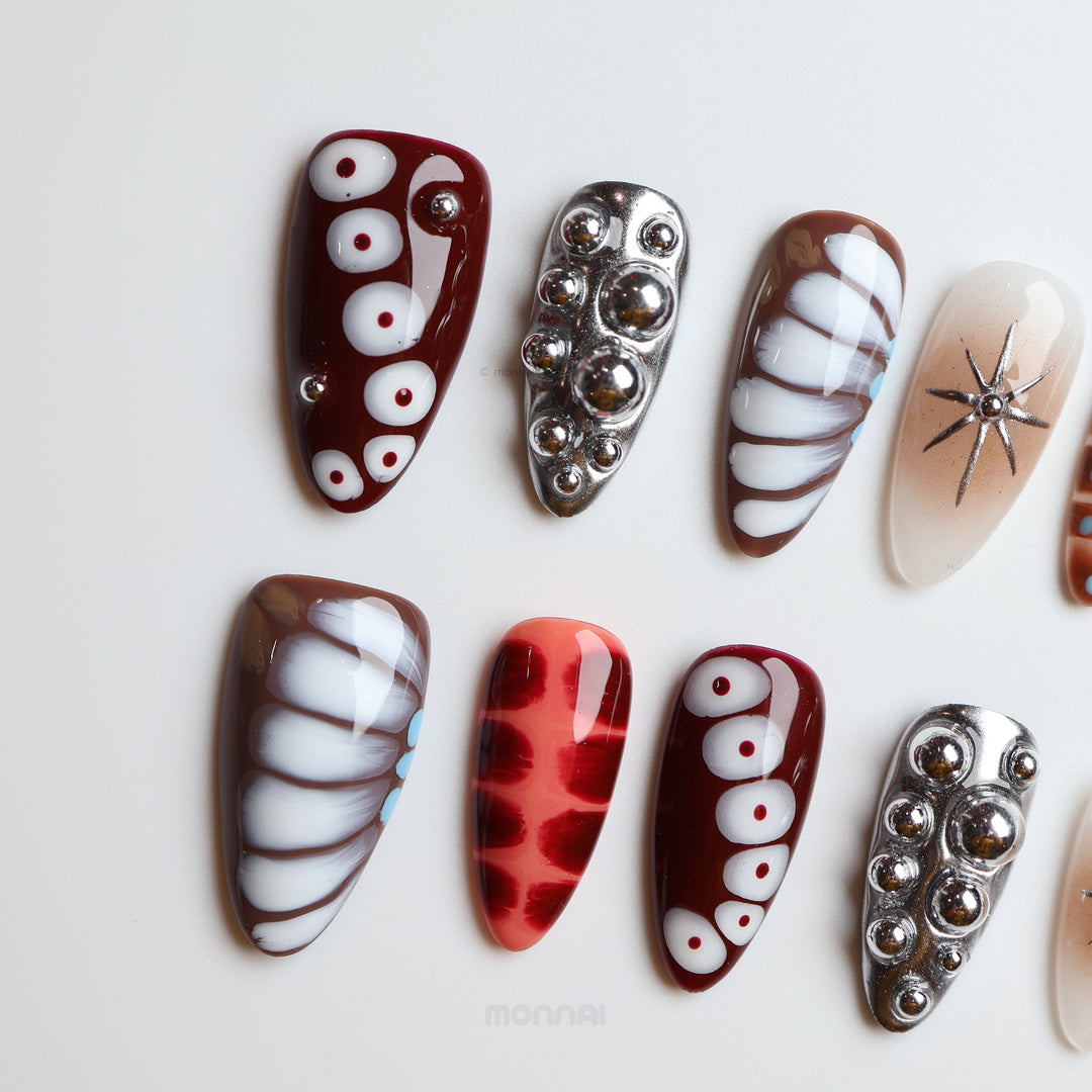 Dark Elegance press-on nails laid out in close-up, with crocodile-print details, chrome spheres, and bold black, brown, cream, and red contrast.