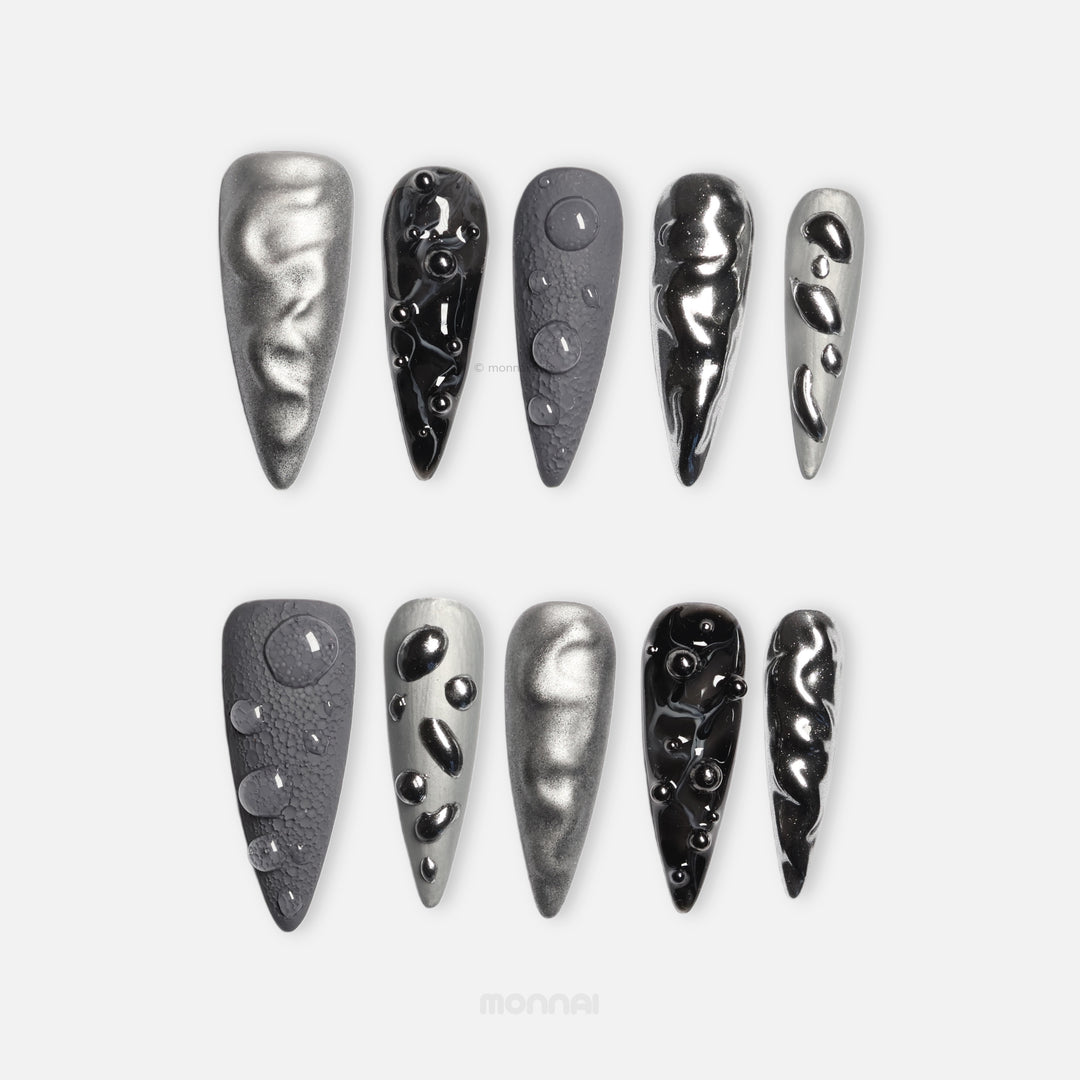 Dark Moon press-on nails laid out in silver, charcoal, and black with crater-like texture and raised gel droplets.