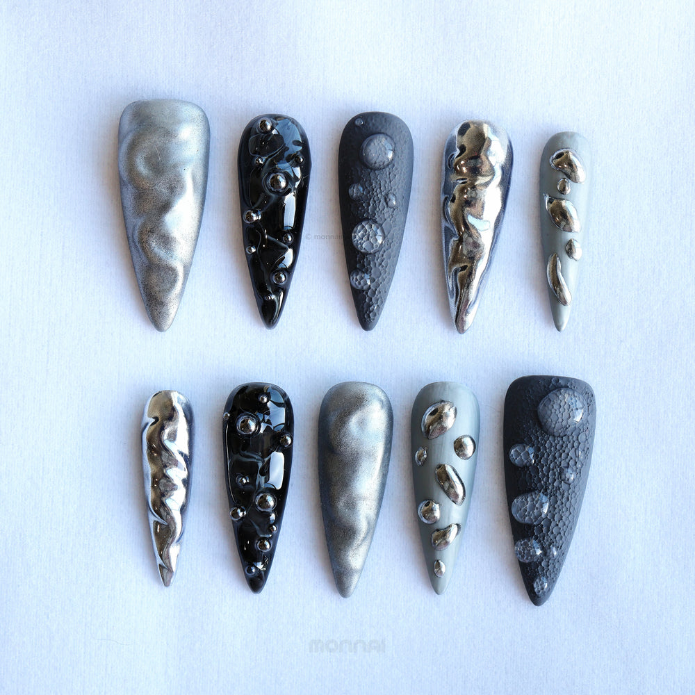 Dark Moon press-on nails laid out in silver, charcoal and black with crater texture and raised gel droplets