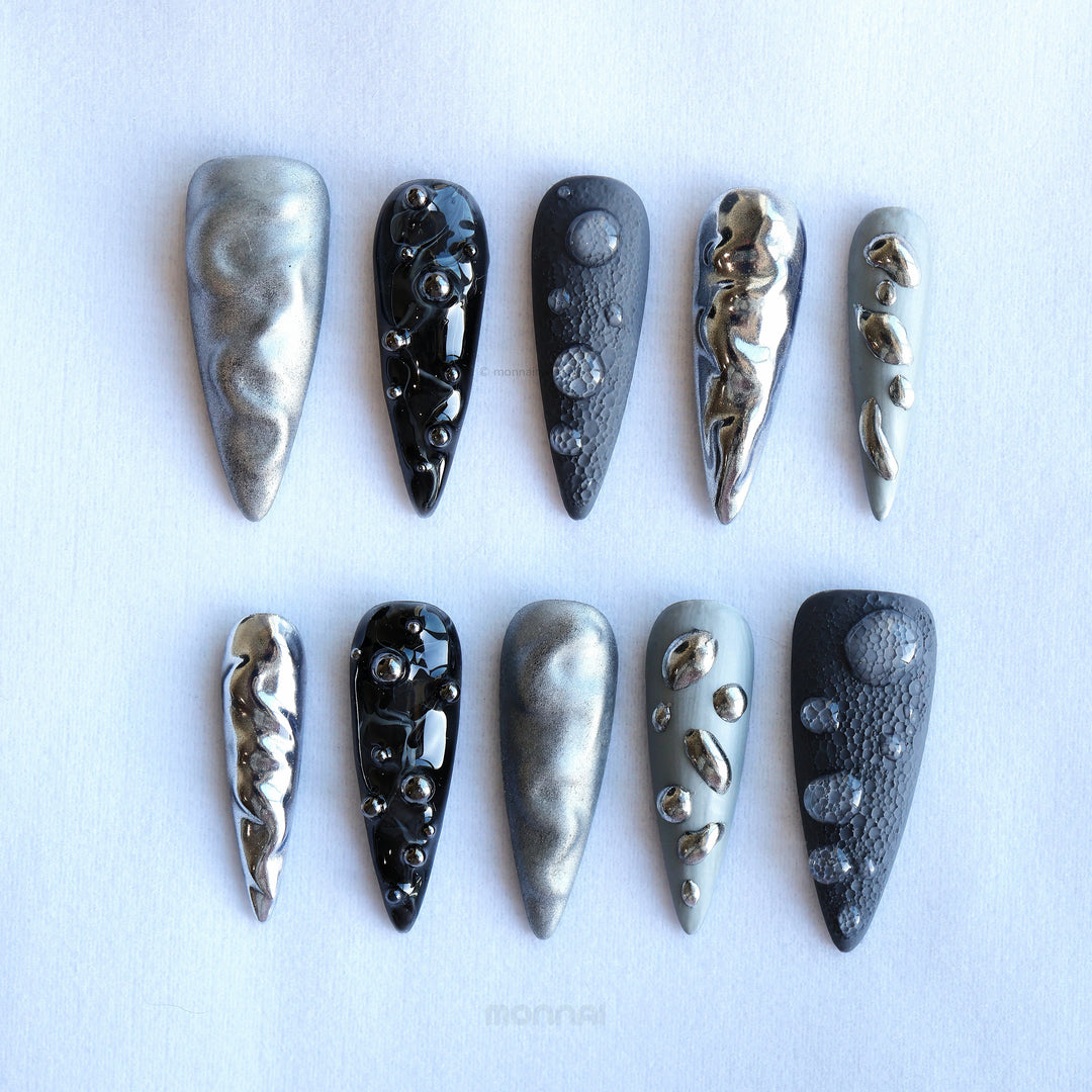 Dark Moon press-on nails laid out in silver, charcoal and black with crater texture and raised gel droplets